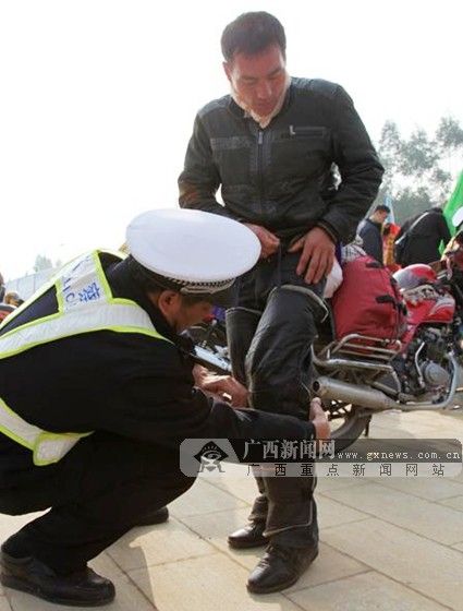 服务点的民警在为长途摩托车队返乡大军中的驾乘人绑好护腿装备。广西新闻网通讯员 谢琴美 摄