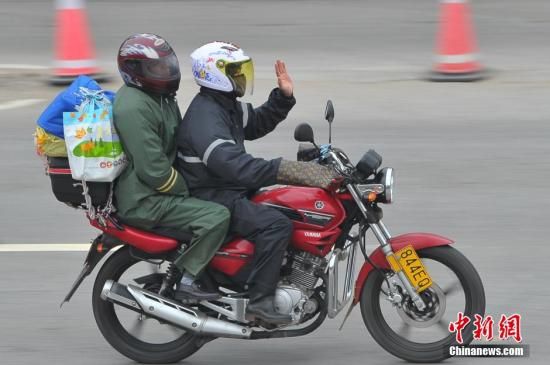  1月25日，从广东驾驶摩托车返乡的务工人员在广西梧州东出口休息站进行休整，图为一名返乡人员在向同伴挥手。中新社发 洪坚鹏 摄 