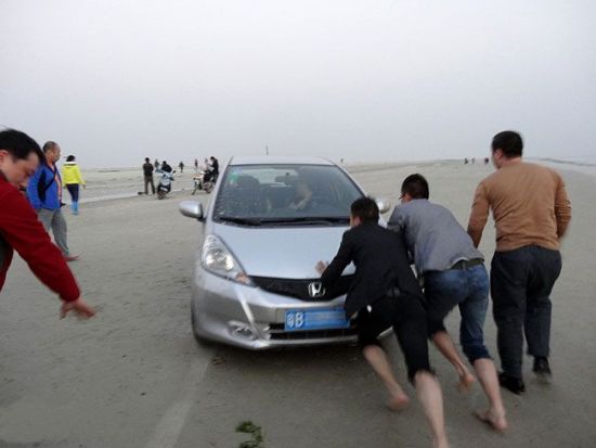 轿车不顾禁令将车开到北海银滩上被陷，北海网友经过努力找来游客将车解救出险地。北海网友阿力供图