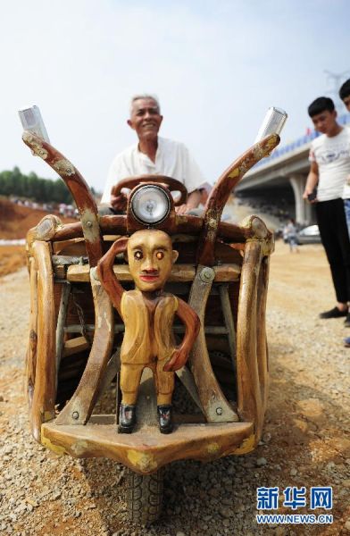 韦贵荣在驾驶自己用樟木手工打造的三轮车，车前脸的木头人眼睛会闪光。