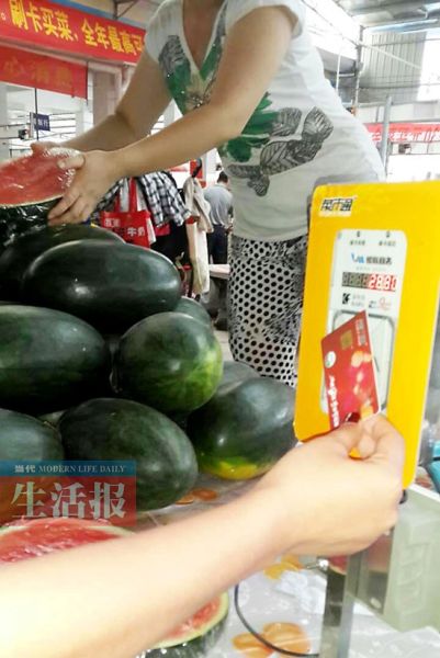 一位市民在苏卢二组农贸市场刷卡买菜。图片来源：当代生活报
